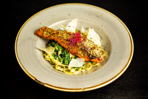 Herb-Crusted Salmon Fillet on a Creamy Spinach Tagliatelle bed, served with Parmesan Shavings